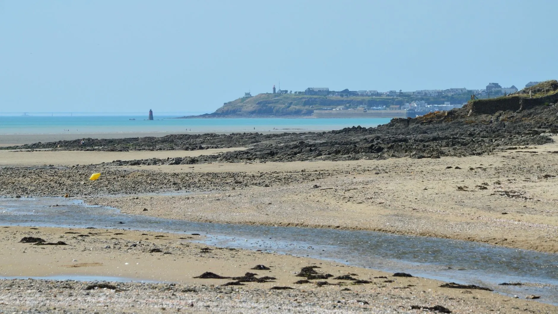 Wide sand flats and a shallow channel at low tide, with a lighthouse and headland in the distance