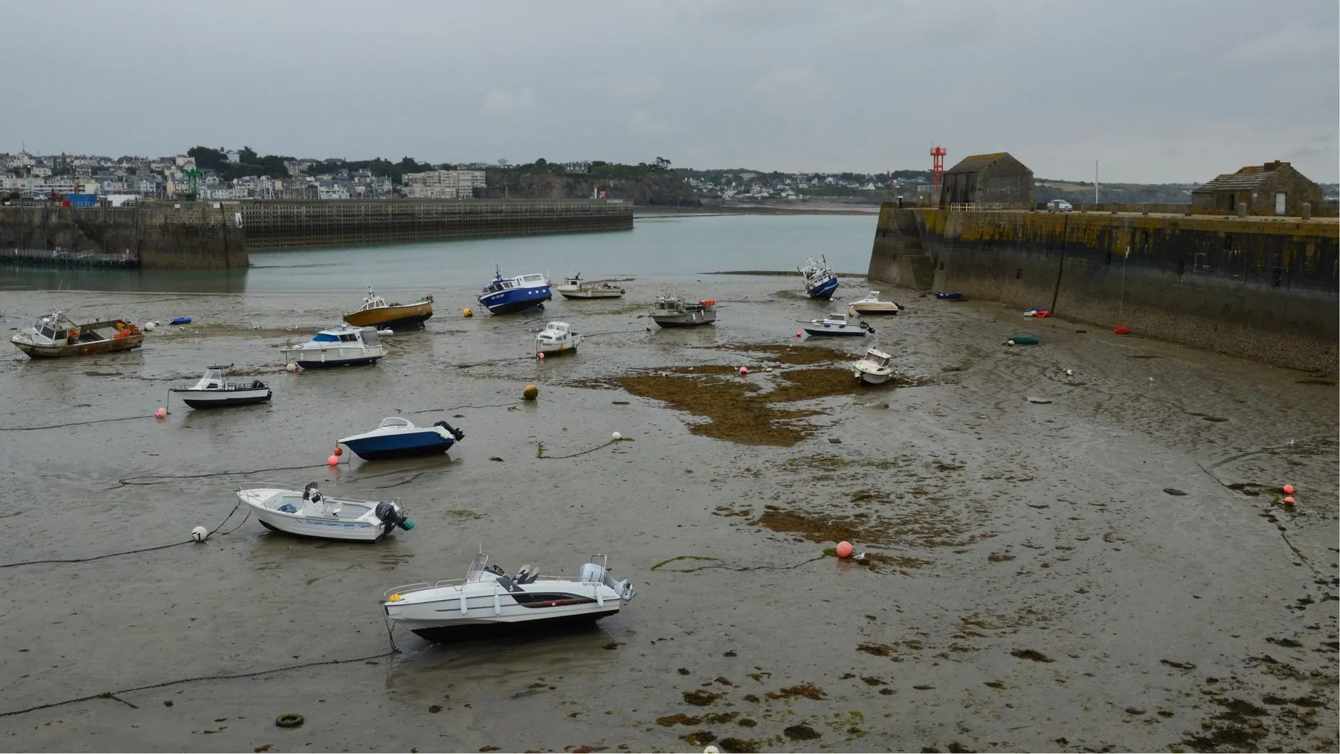 Small motor boats lying on the mud of a walled estuary basin at low tide, mooring lines slack