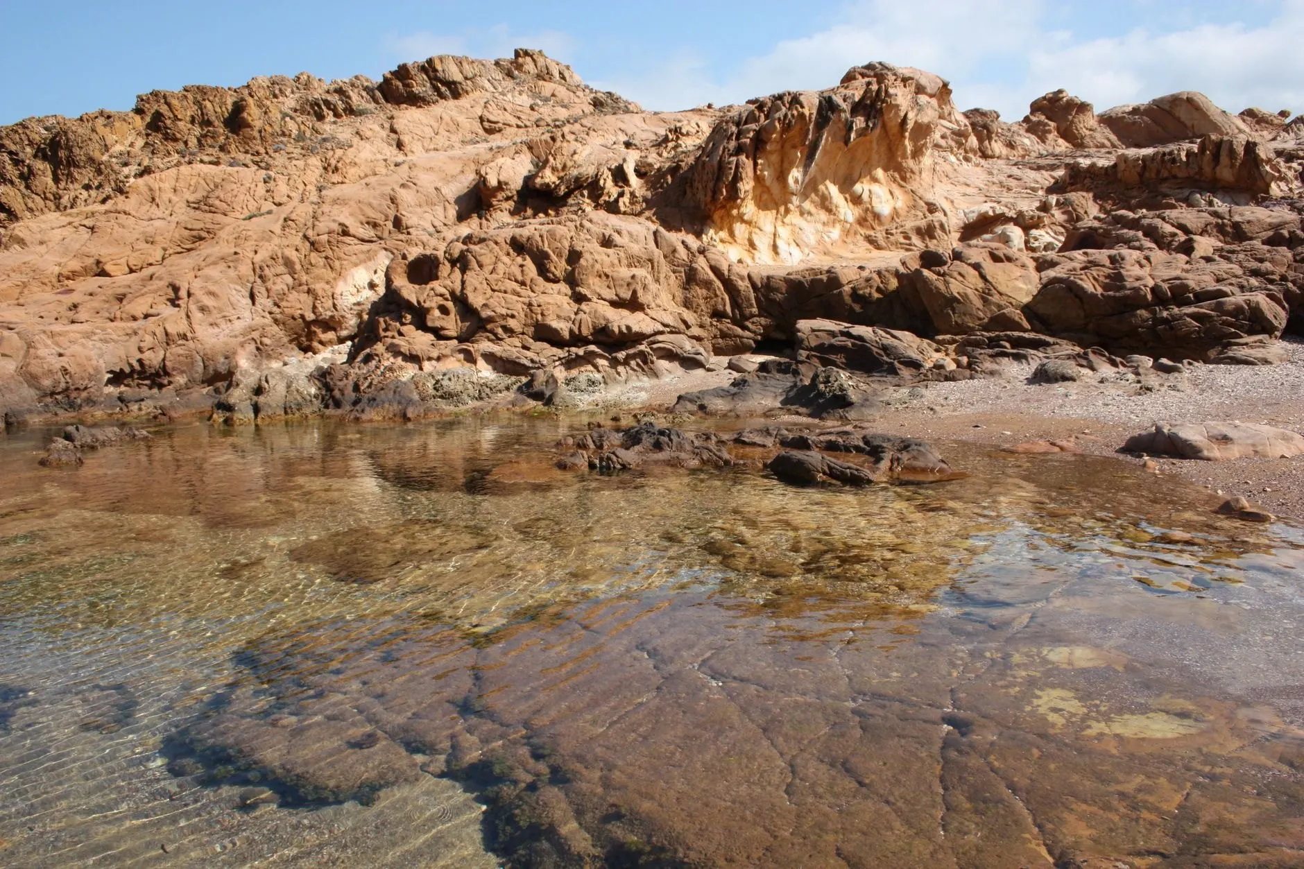 A clear tide pool among weathered orange rocks at low tide