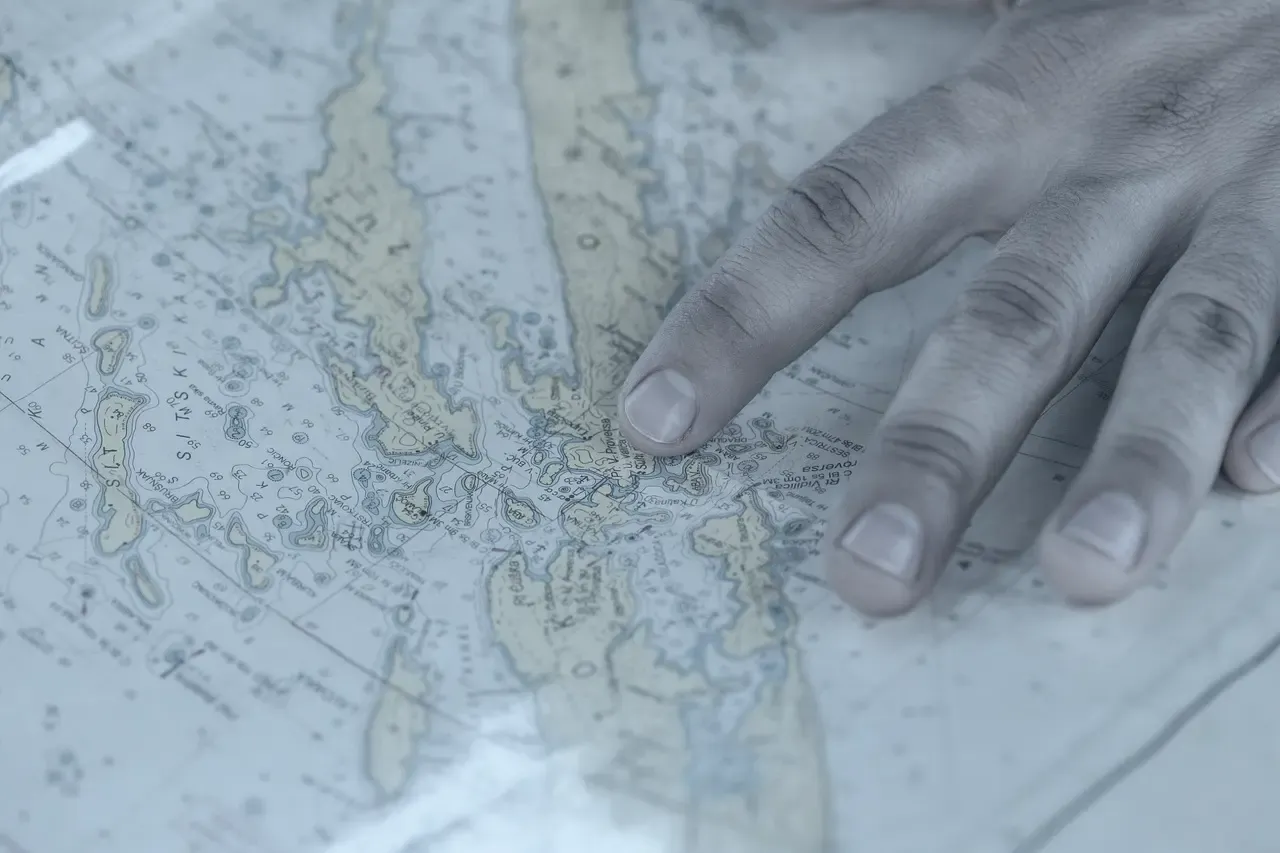 A hand resting on a paper chart while a passage is planned.