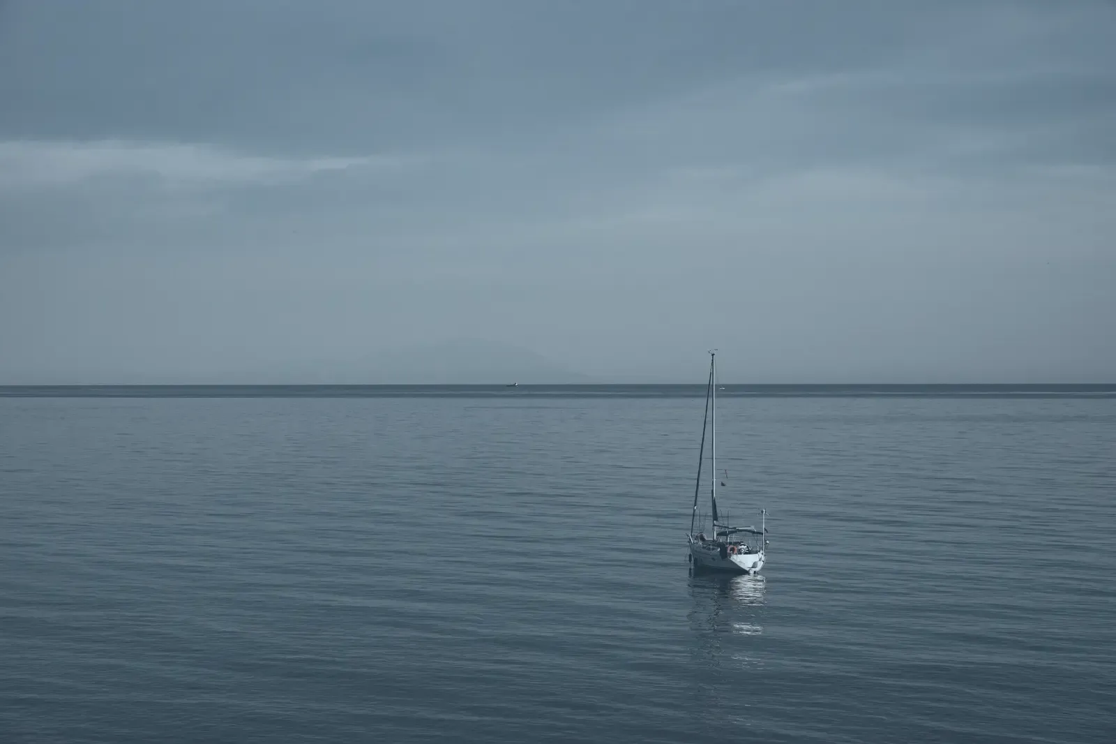 A single yacht on flat calm water at dusk, well offshore.