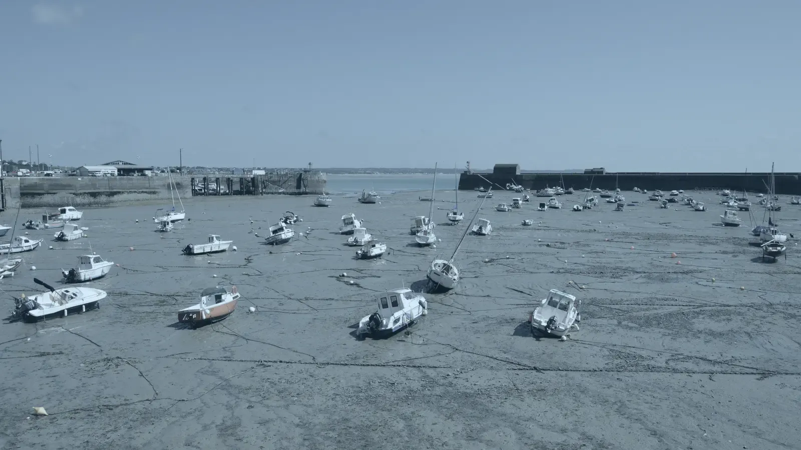 A tidal harbour at low water, the moored boats sitting on the mud inside the wall.