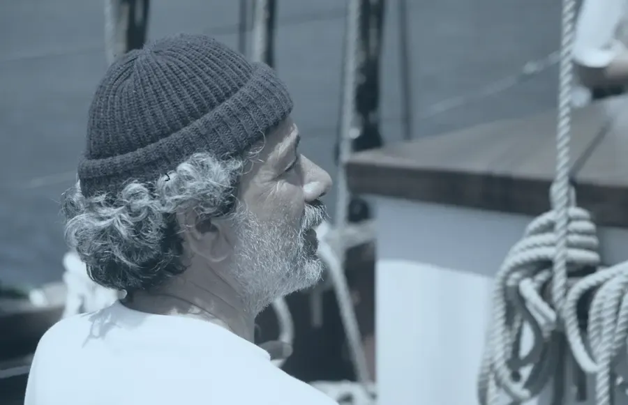 A skipper on deck, looking out along the coast.